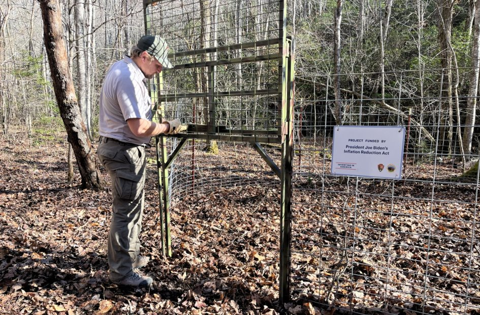 A uniformed worker stands in front of a metal trap enclosure with a sign on it.