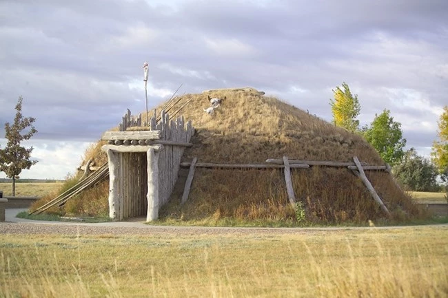 A grass-covered, dome-shaped earthlodge with a timber-framed doorway