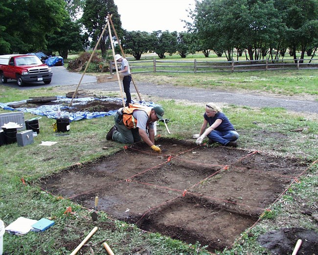 Archaeologists working in a shallow excavation.