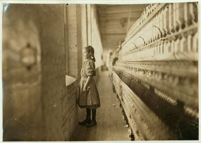 A young girl spinner standing at a mill window, 1908