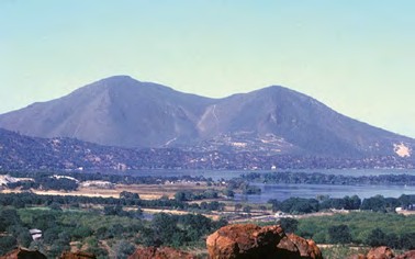 Dos cerros volcánicos redondeados sobre un lago y una llanura con casas, en Clear Lake Volcanic Field