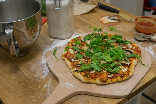 Image of a pizza peel with mushroom and arugula.
