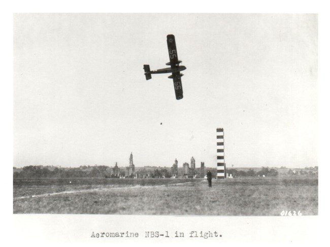 An Aeromarine NBS-1 flying past a pylon, with a mock-up of New York City behind it for a bombing demonstration.