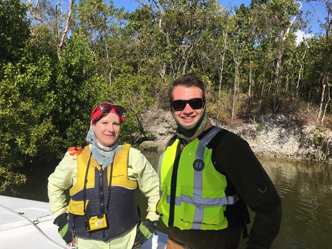 Two archeologists in safety vests smiling for the camera