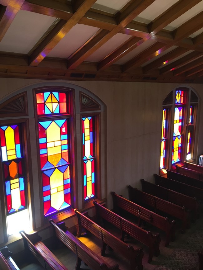 Sanctuary pews seen from the organ loft, facing a three-part geometric stained glass window.