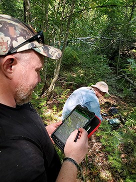 A researcher checks an amphibian acoustic recorder while a colleague logs data on a tablet.