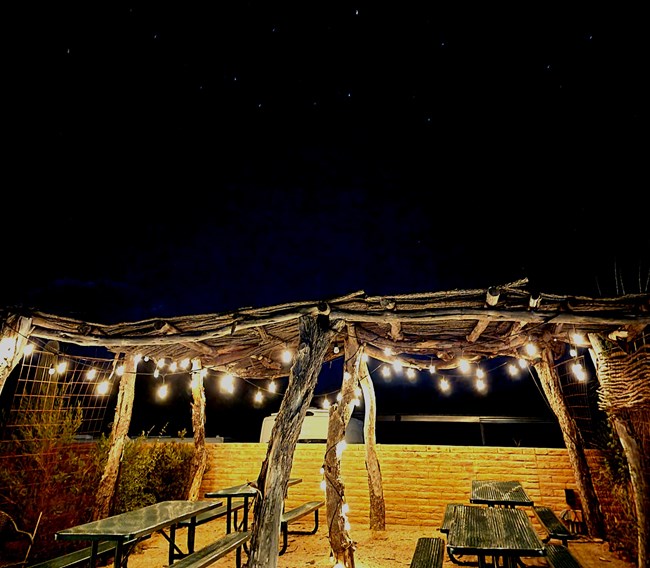 A ramada with string lights above picnic tables under a night sky.