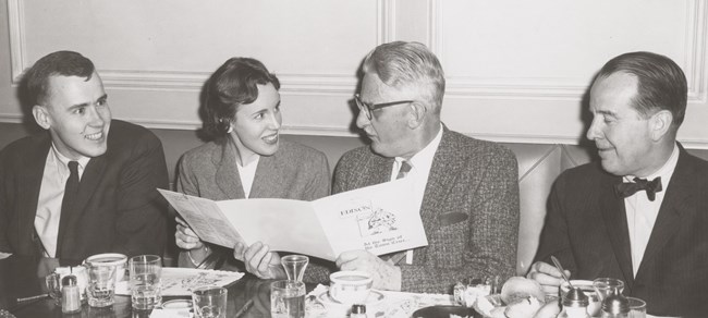 James C. Massey, Anne Massey, R.A. Wilhelm and Charles E. Peterson at a dinner table looking at a brochure.