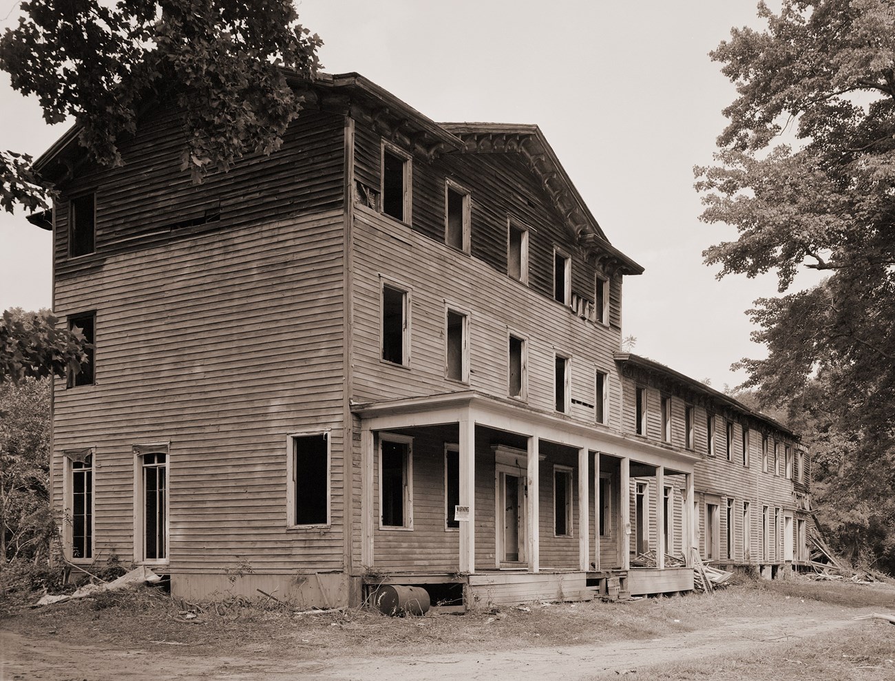 A three-story wooden building with every window broken, and a two-story wing on its right