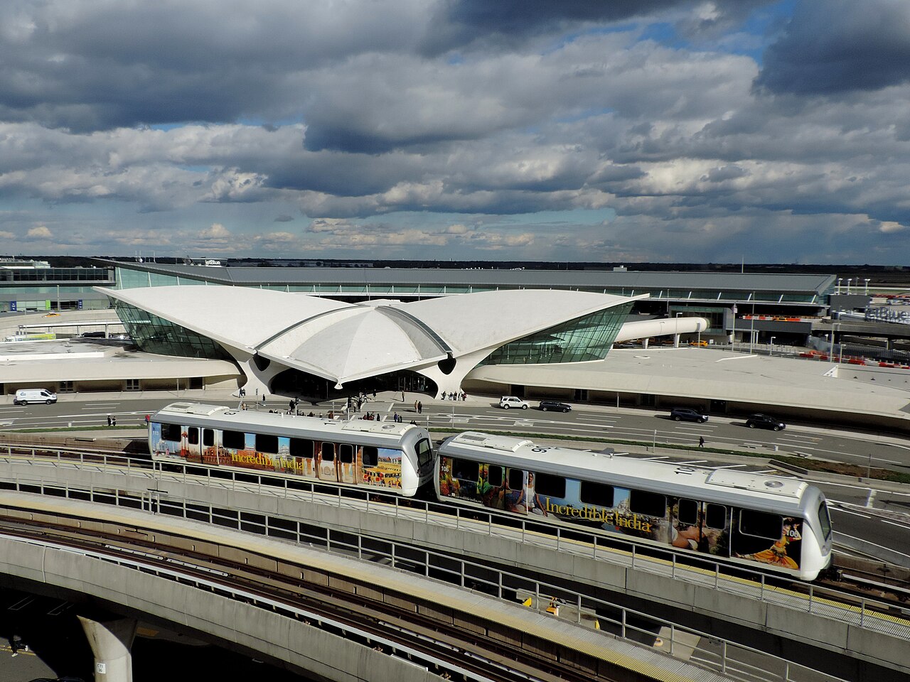 AirTrain JFK আইকনিক TWA ফ্লাইট সেন্টারের পাশে অতিক্রম করছে, যা টার্মিনাল ৫-এর প্রধান ভবন, ইরো সারিনেন দ্বারা ডিজাইন করা।
