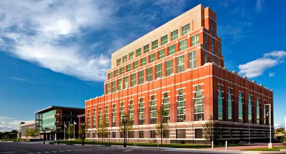The tall brick power plant with stepped roofs and long vertical windows, its walls shading from darker at the base to lighter at the top, seen from the street under a blue sky.