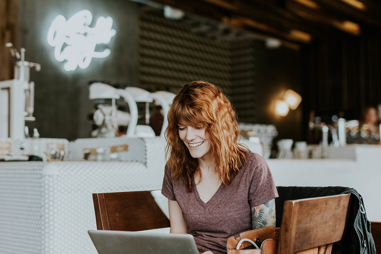 A photograph shows a woman on a laptop while she sits at a coffee shop.