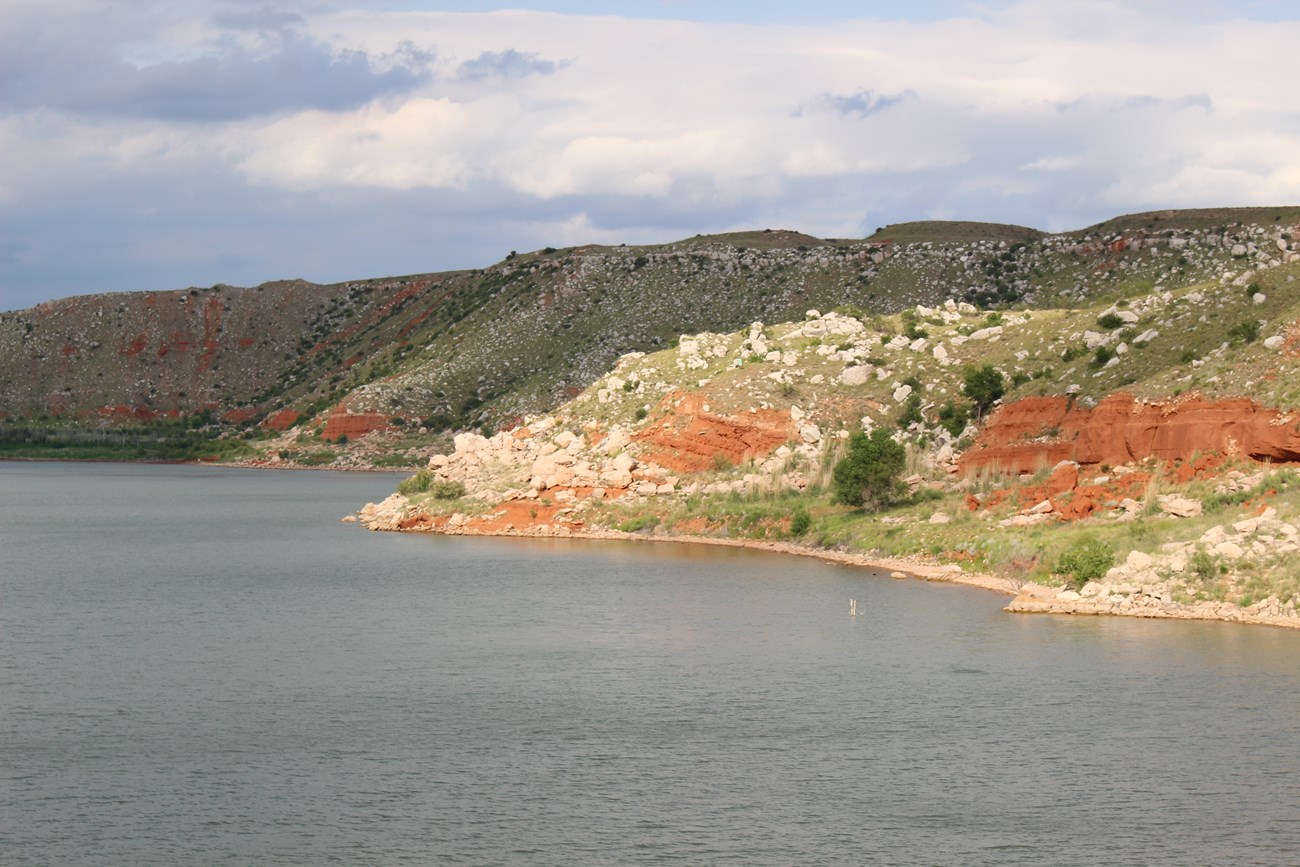 Lake shore below rocky bluffs, with white boulders scattered down red slopes.