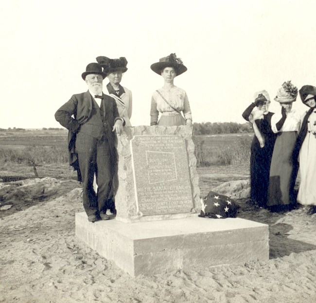 A man and women standing beside a stone marker, in black and white.