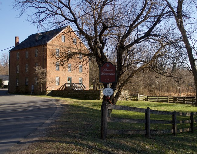 A brick mill building beside a road sign reading Welcome to Waterford