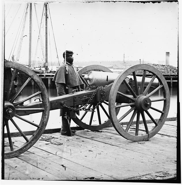 A Black Civil War soldier standing guard beside a cannon.
