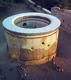 The round adobe mortuary chapel seen from above, with a cross beside it