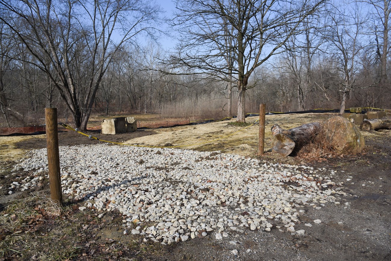 Where the house at 3132 Akron Peninsula Road stood, removed in 2021: a gravel drive, fence posts and straw-covered ground among bare trees, the land now being reforested.