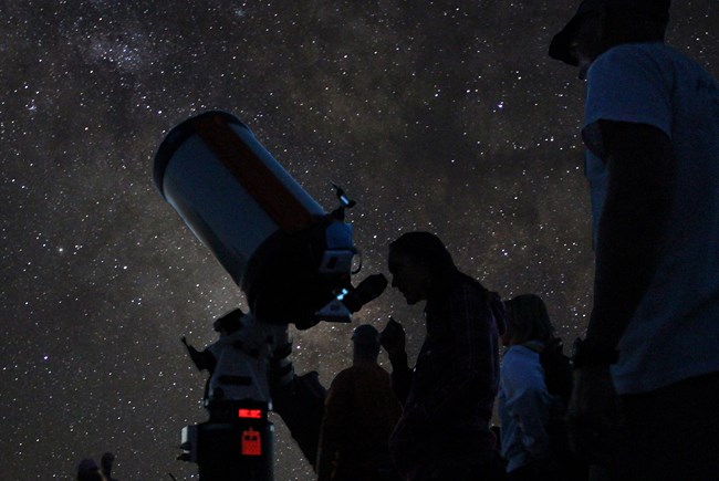 Silhouetted visitors at a large telescope under a starry sky