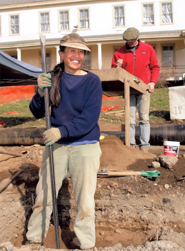 A smiling woman holding an archaeological tool.