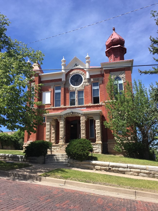 A red brick synagogue with an onion-domed tower, a large round central window and small minarets, on a steeply sloping corner lot.