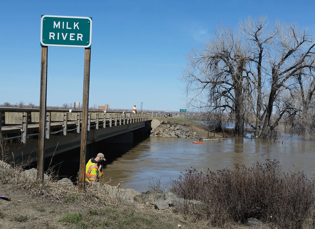 Photograph of the Milk River from a bank near a bridge, with scientists sampling.