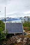 A solar-powered station on a rocky island with a glacier behind