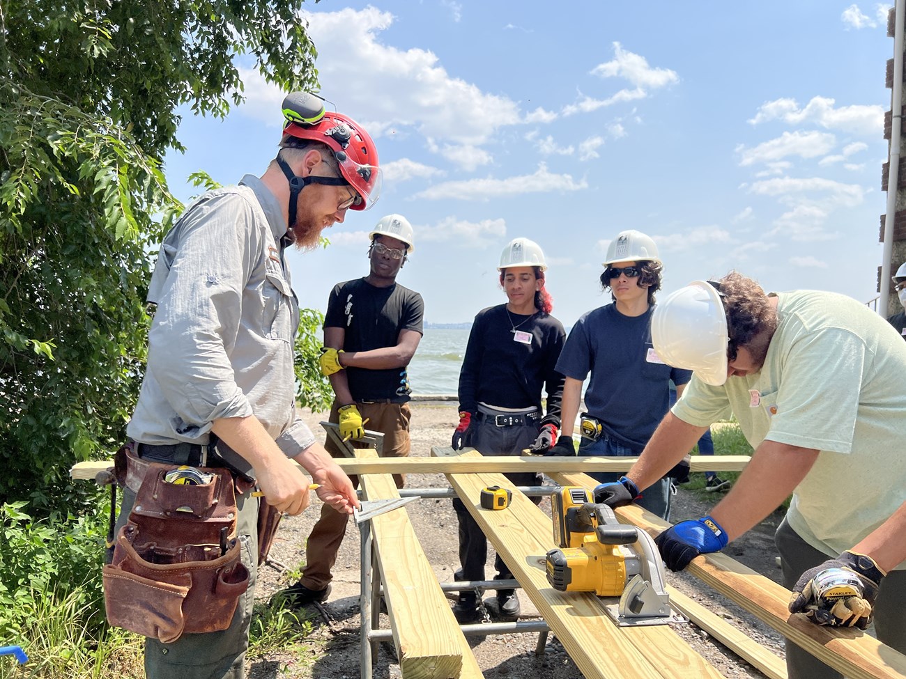 A group of interns and park staff in hard hats around a circular saw.