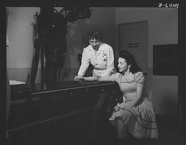 A nurse positions a seated woman's right wrist on an X-ray machine