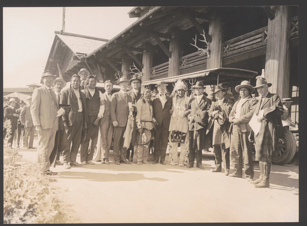 Men in suits and Blackfeet men in front of a large log building