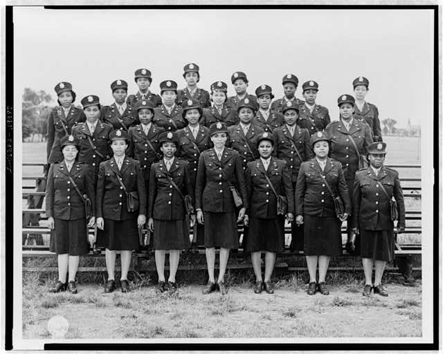 Twenty-four Black Army nurses in dark uniforms and caps, standing in four rows.