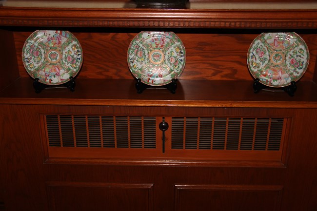 Three Famille Rose plates displayed on a shelf in the Mansion's hallway.