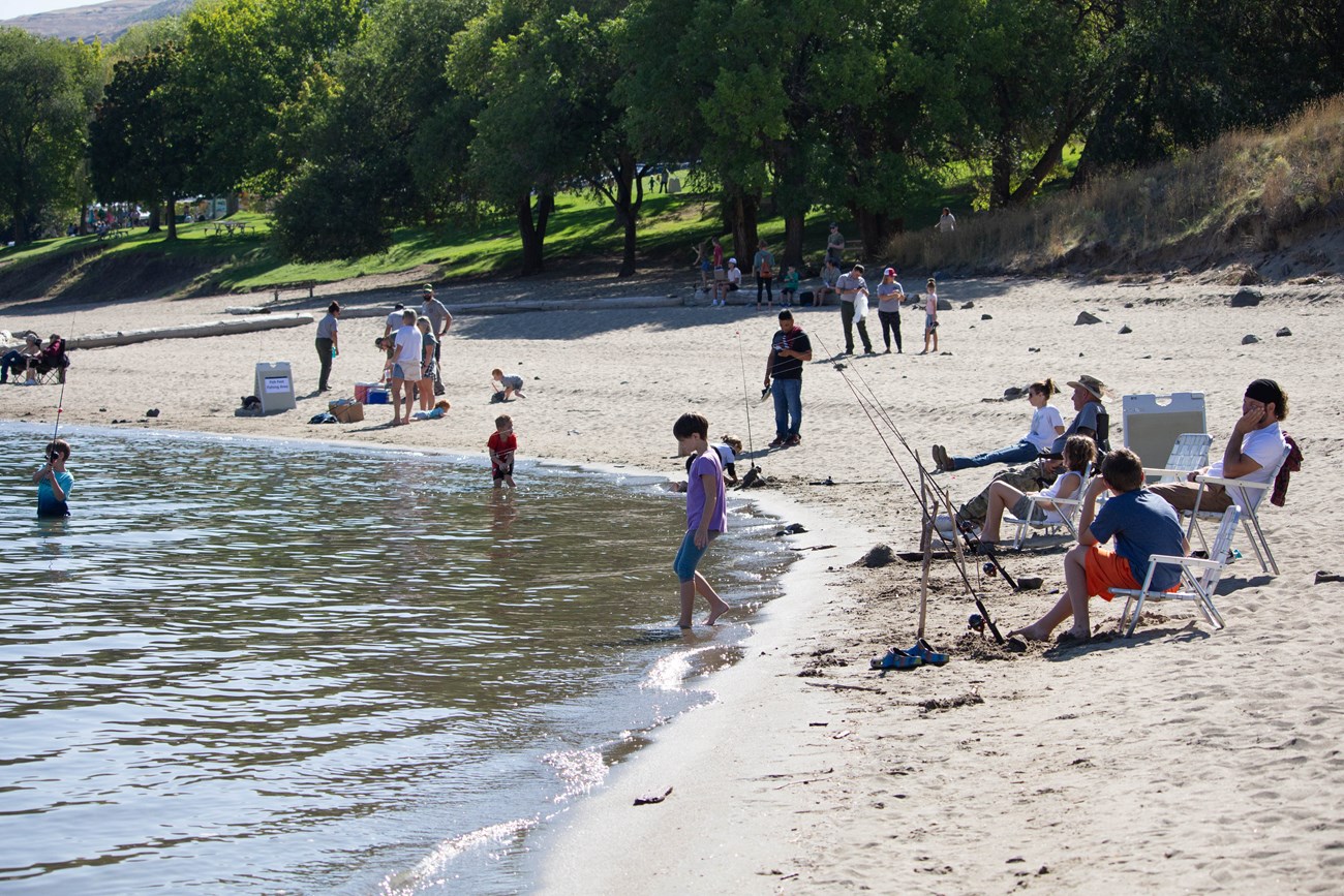 Children and adults along a sandy beach, many of the children fishing from the shore.