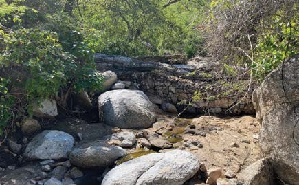 A rock gabion across a dry stream channel strewn with boulders