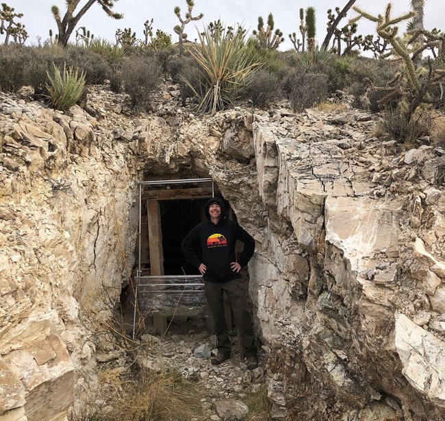 A man stands beside a harp trap at the entrance of an abandoned mine.