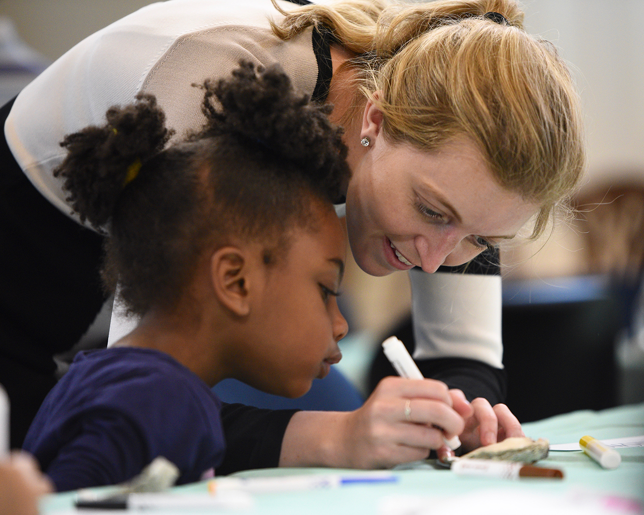 A photograph shows a woman using markers to color with a child.