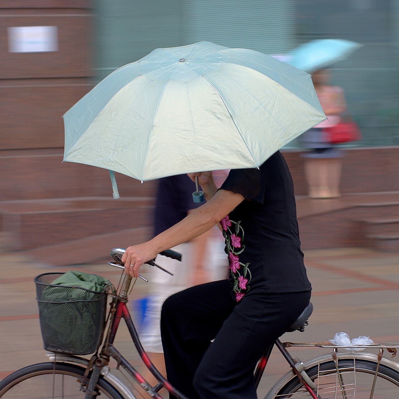 Woman cycling in the rain holding an umbrella