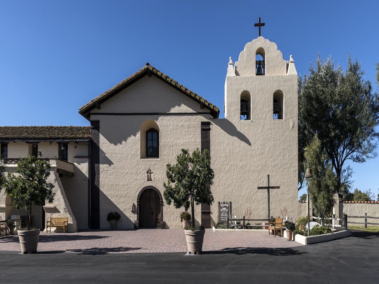 A tan mission church with a bell tower beside it, trees in front