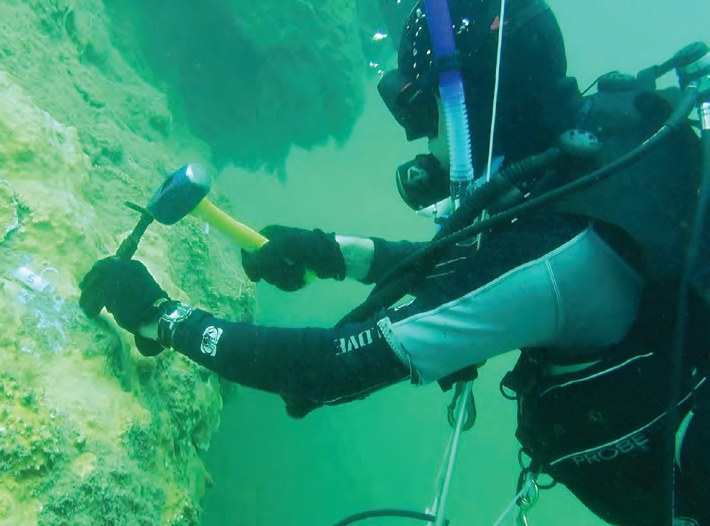 A diver on a reef using a hammer and chisel to take a sample of coral