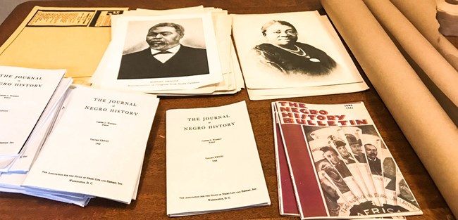 A desk covered with rolls of paper and piles of pamphlets.