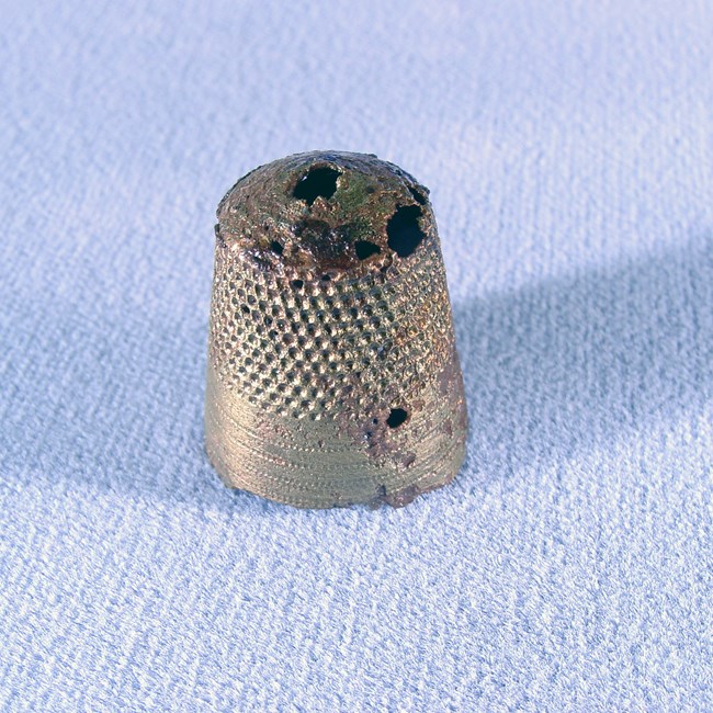 A textured brass thimble with holes punched through it.