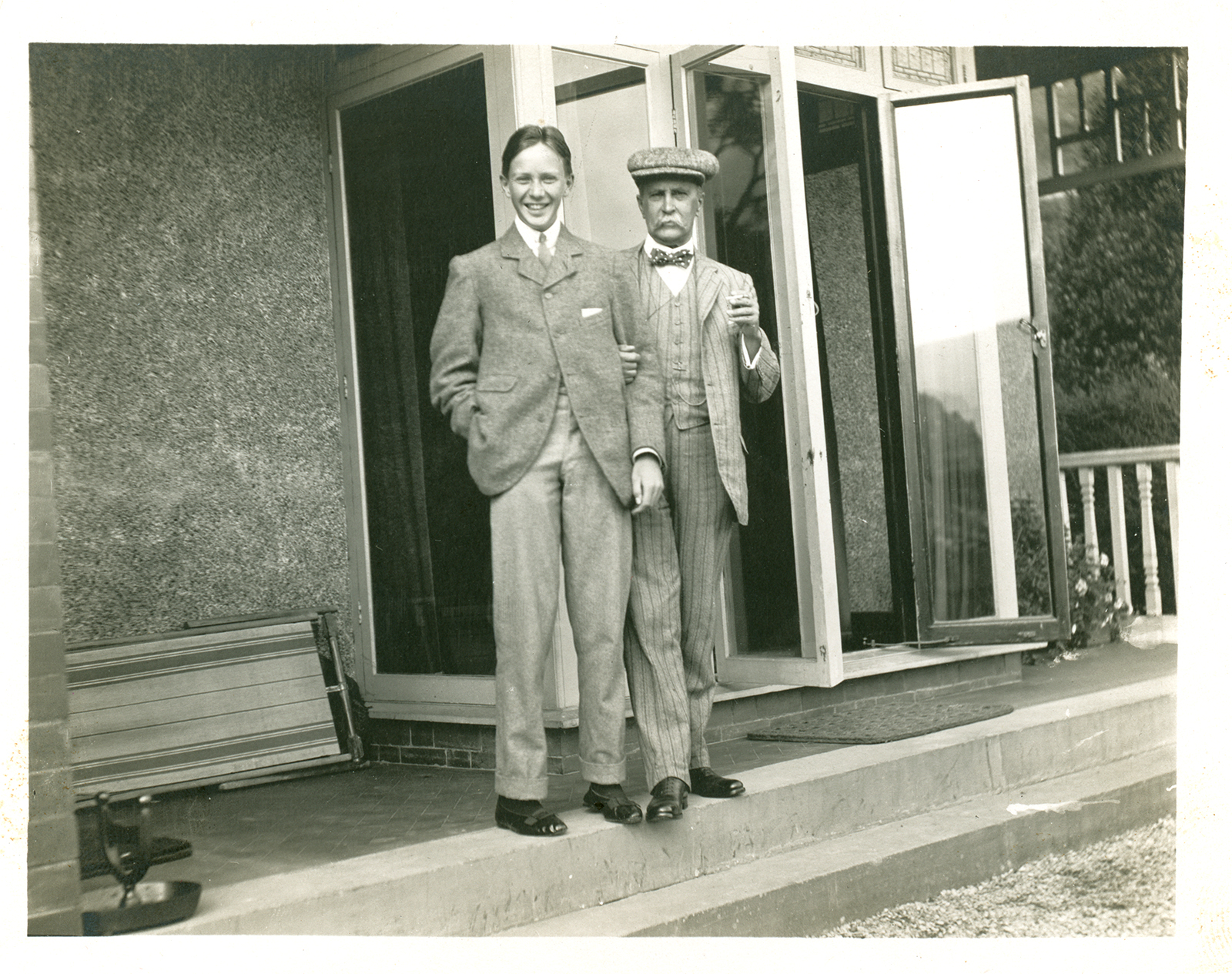 An older man and a teenage boy post together on a porch.