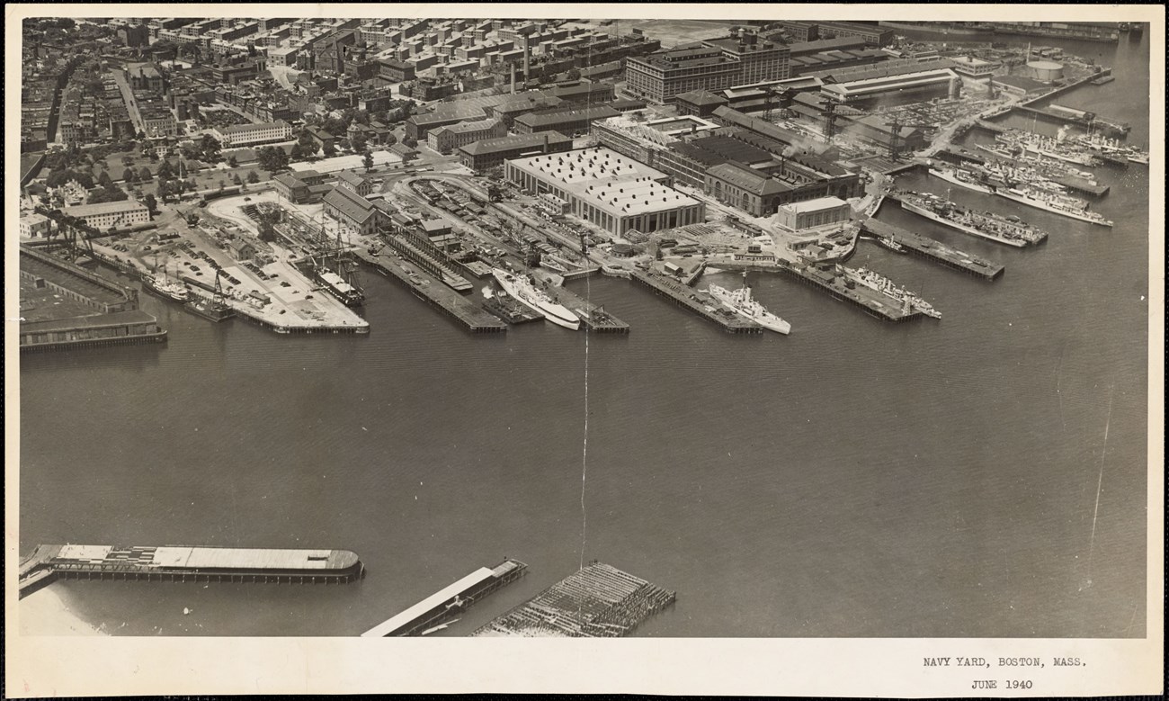 Black-and-white aerial photograph of the Charlestown Navy Yard in 1940, its piers crowded with ships and the town of Charlestown behind.