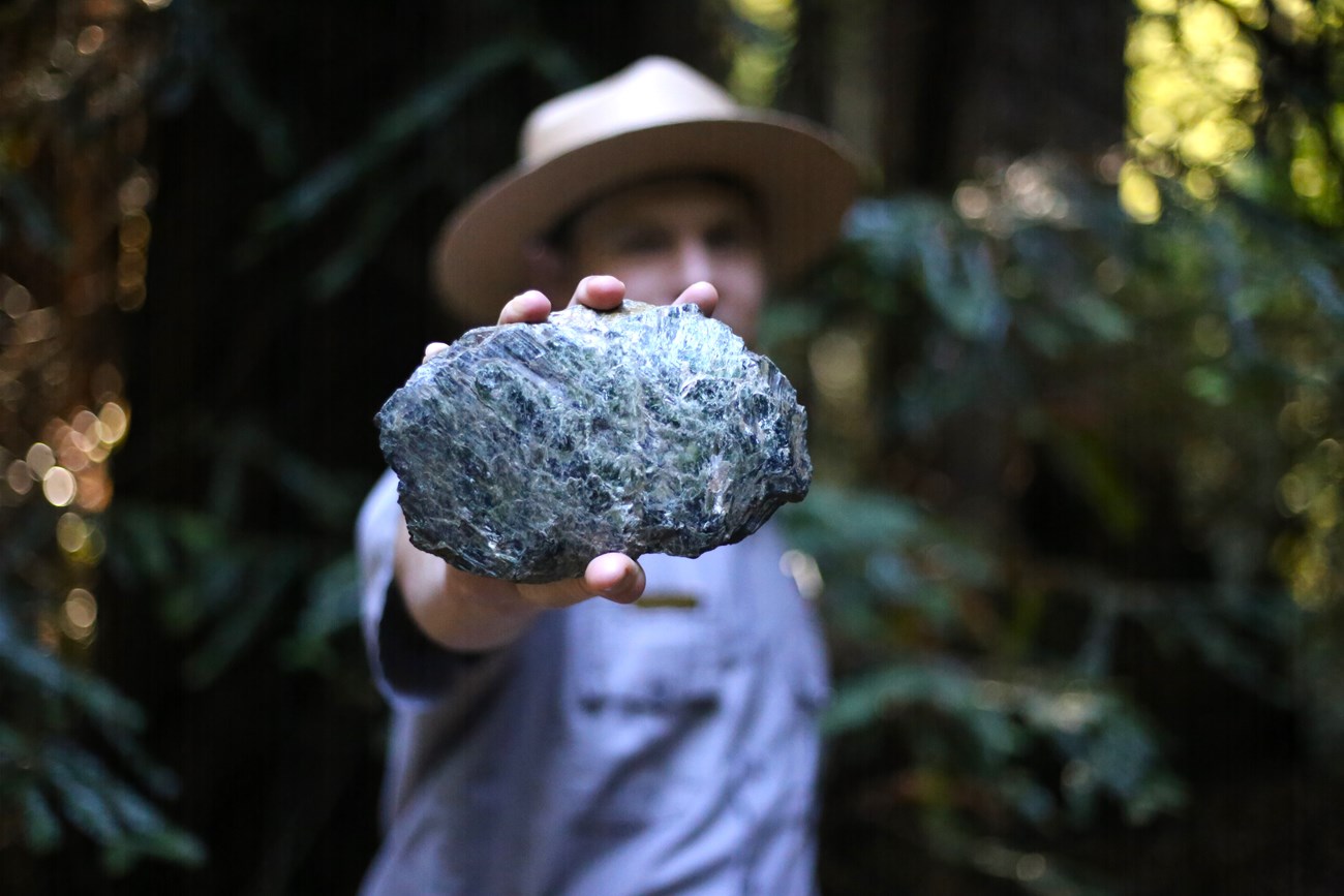 A ranger holding a chunk of greenish-gray rock