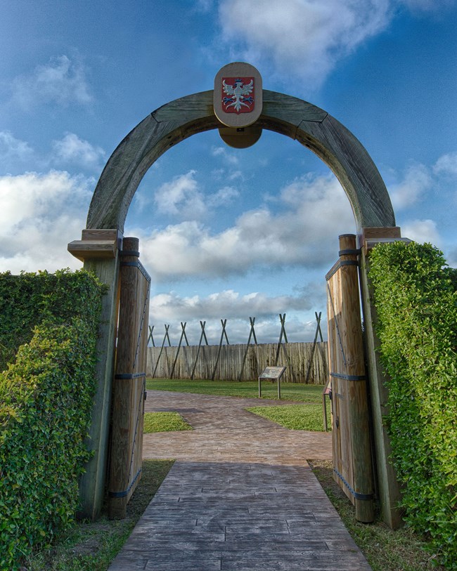 A wooden arched gateway opening onto a reconstructed palisade fort.