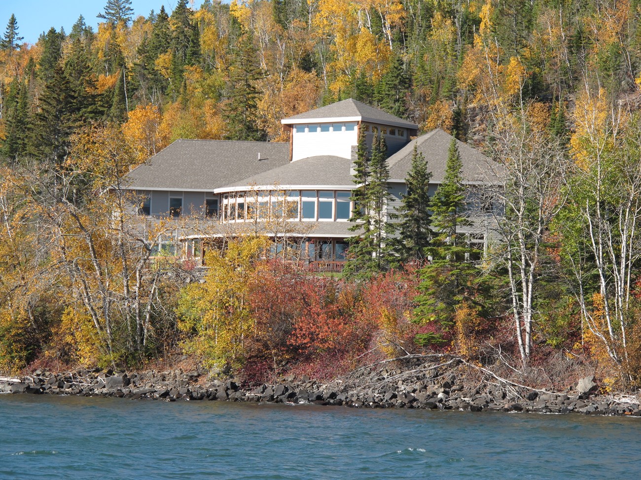 A building with many windows on a hill among fall-colored trees.