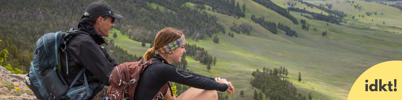 a smiling man and young woman rest on their hike, enjoying the view
