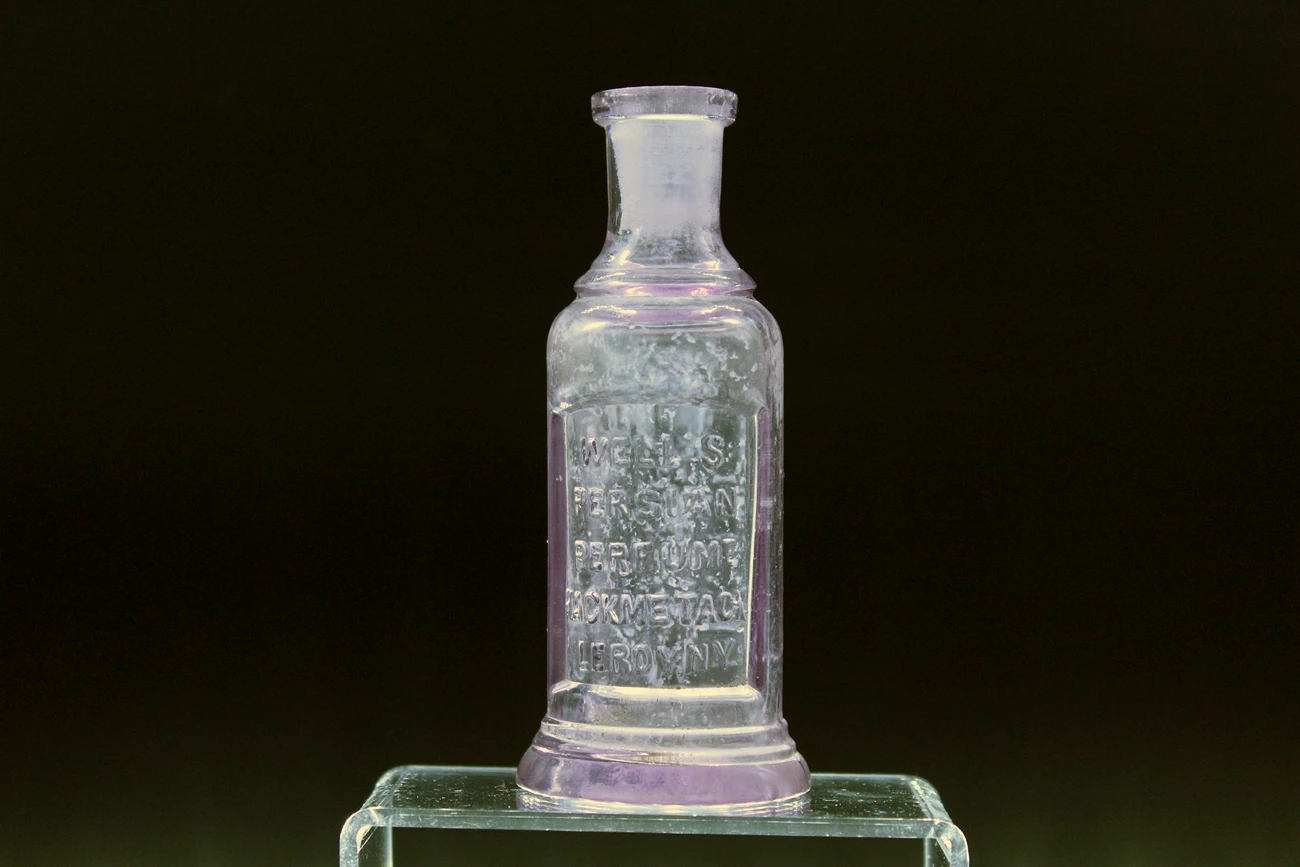 A small glass bottle with embossed lettering on a clear stand.