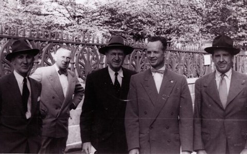 Five men in suits in front of an iron fence.