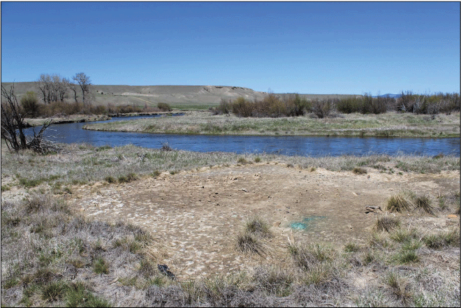A stretch of river with a bare patch of dirt on the bank where grass is missing.